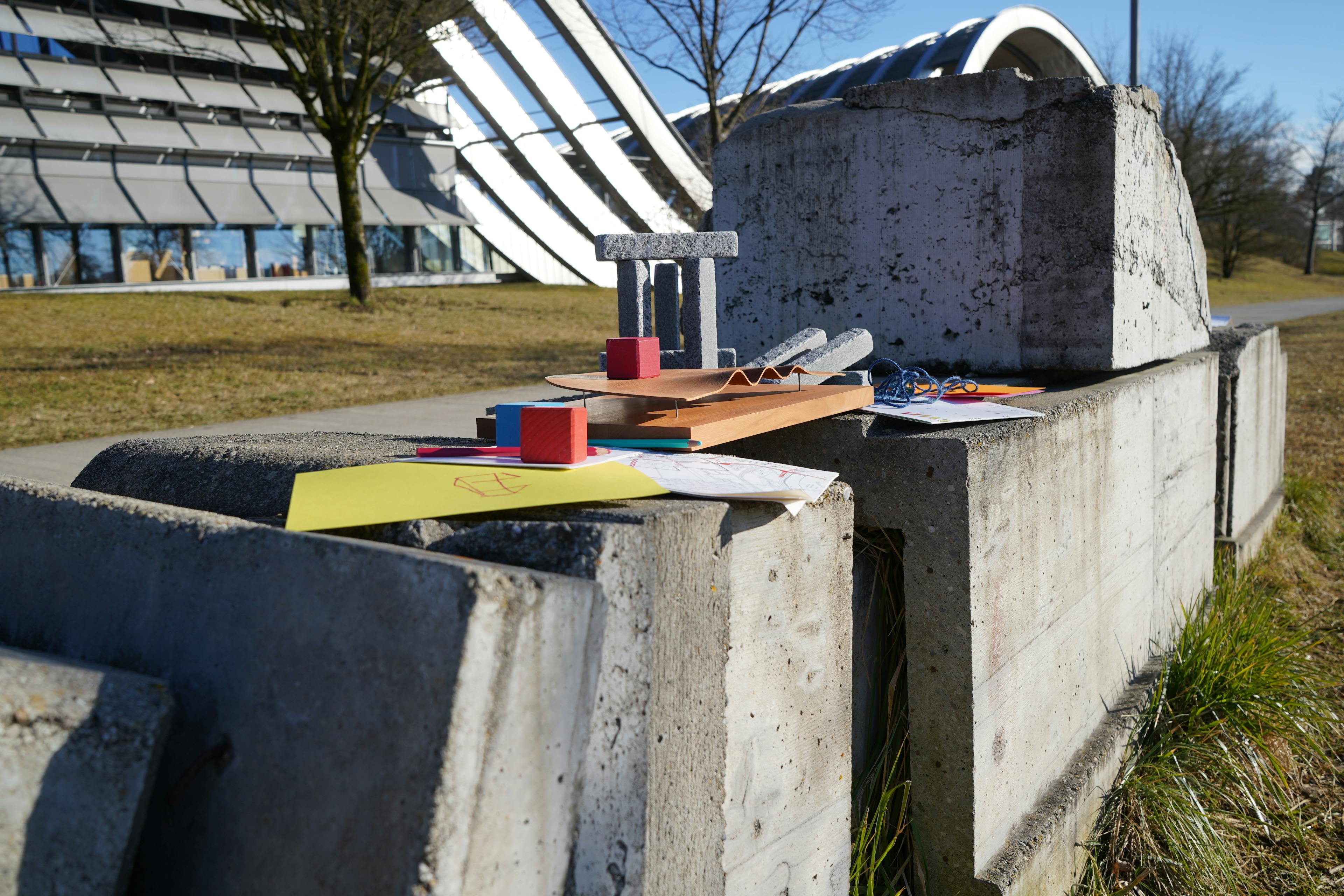 Steinskulptur vor dem Zentrum Paul Klee mit einfachen, farbigen Holzmodellen und einem Zeichnungsblock im Vordergrund