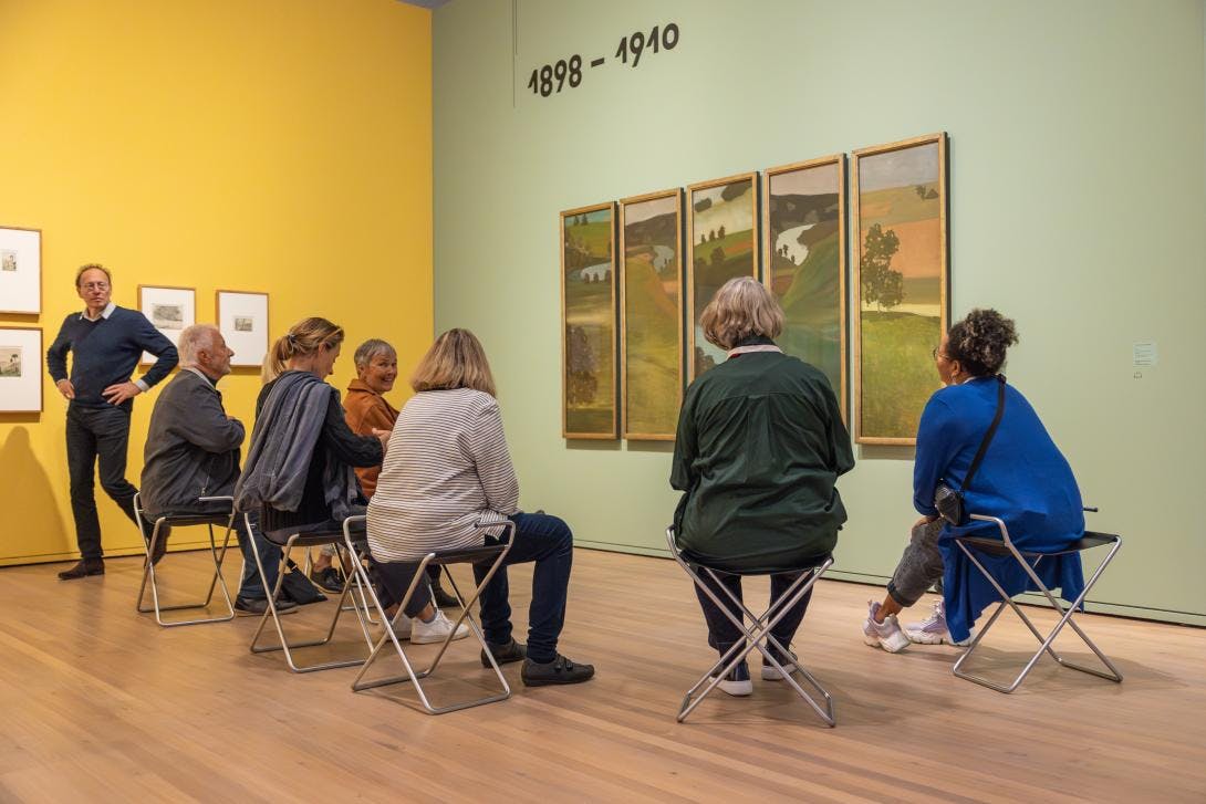 Eine Gruppe von Menschen sitzt nahe um ein Werk von Paul Klee und betrachtet dieses eingehend. 