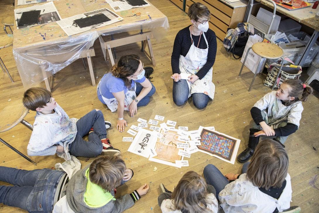 eine Gruppe von Kindern und Erwachsenen sitzt im Kreis am Boden und trägt Stichworte zu Werken von Paul Klee zusammen, die sie auf kleinen Zetteln festhalten.
