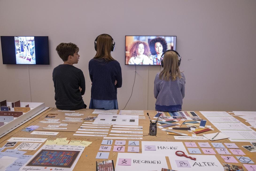 Kinder erkunden die Ausstellung Leuchtendes Geheimnis. im Vordergrund des Bildes sieht man einen Tisch auf dem diverse Materialien aus dem Entstehungsprozess der Ausstellung zu sehen sind.
