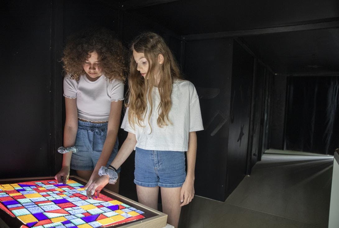 Zwei Mädchen erkunden über ein Tastrelief das Werk Glasfassade von Paul Klee.