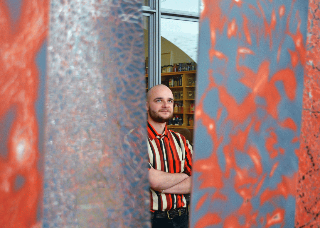 Kunstwerk in Orange und Graublau, in der Mitte des Fotos steht Lorenz Fischer, Kunstvermittler im Creaviva