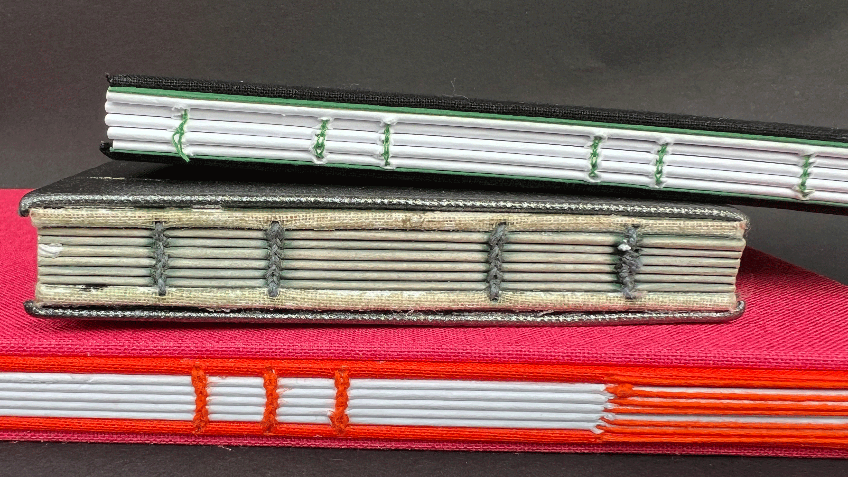 Drei Buchrücken sind im Vordergrund, die mit unterschiedlichen Techniken des Buchbindens gestaltet sind.