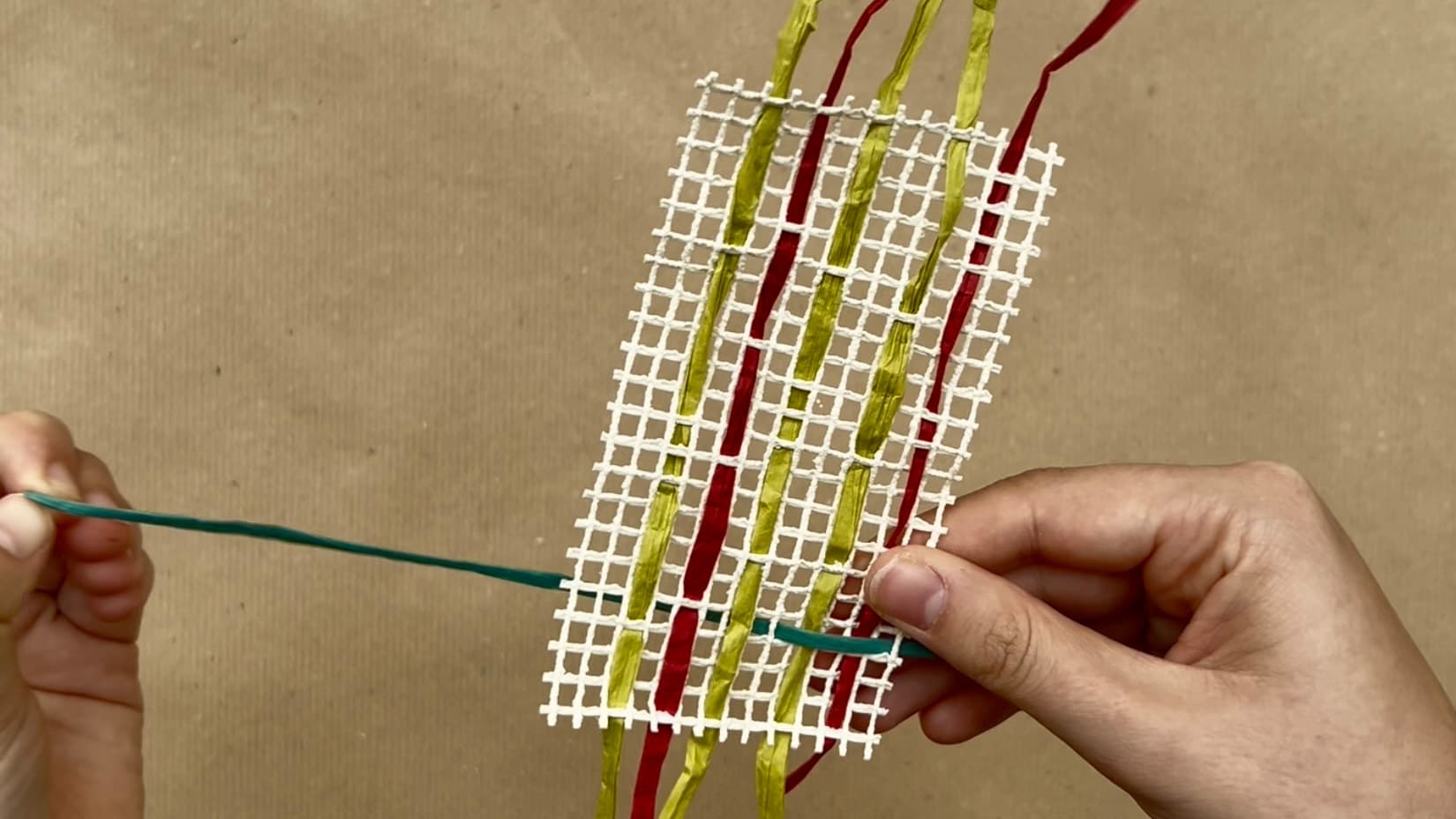 In einem quadratischen Netz werden bunte Fäden verflochten.