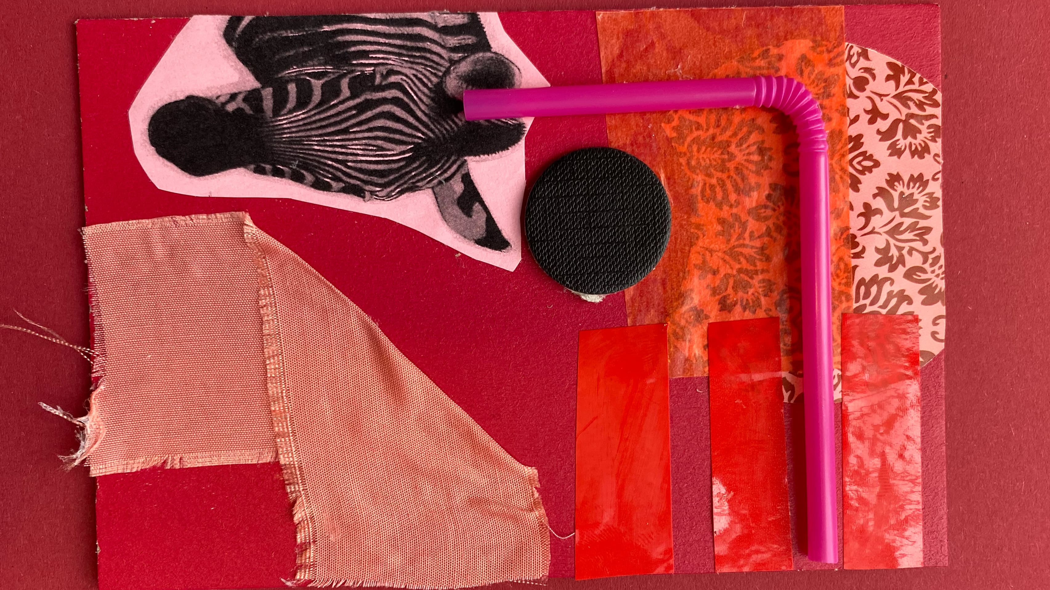 Eine Collage in Rottönen aus unterschiedlichen Materialien: Strohhalm, Stoff, Papier.